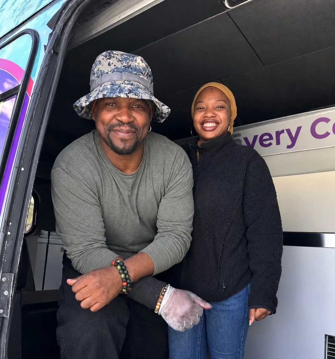 Two community volunteers smile together beside a service vehicle.