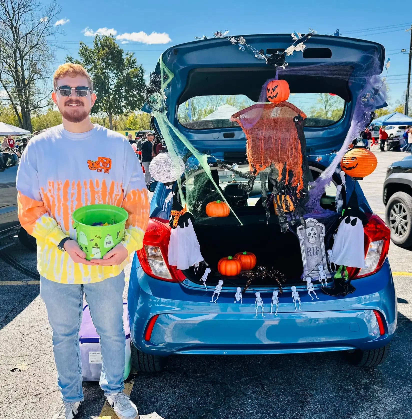 A community volunteer stands beside a decorated trunk-or-treat vehicle.
