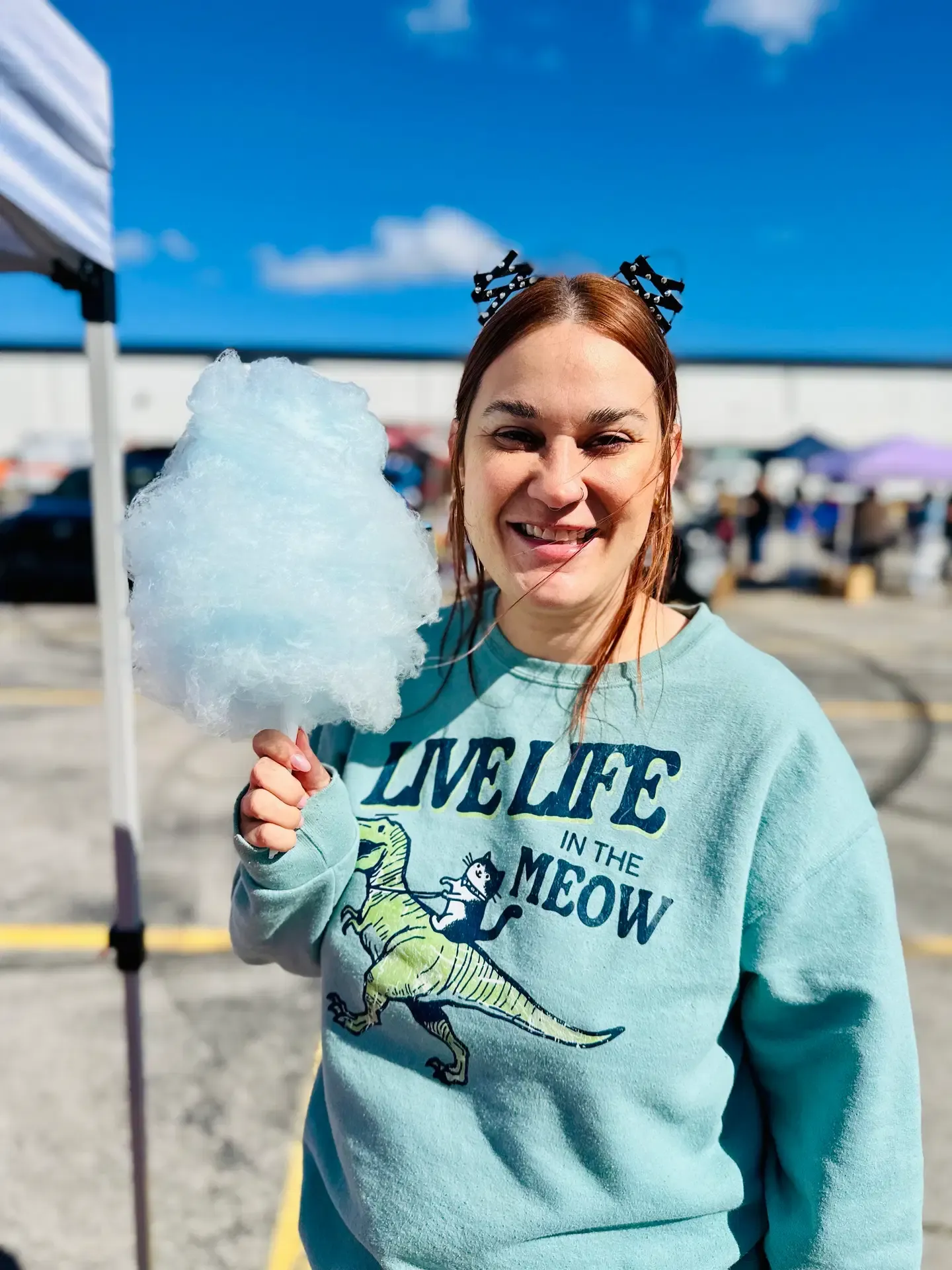A festival guest enjoys cotton candy beneath a vendor tent.